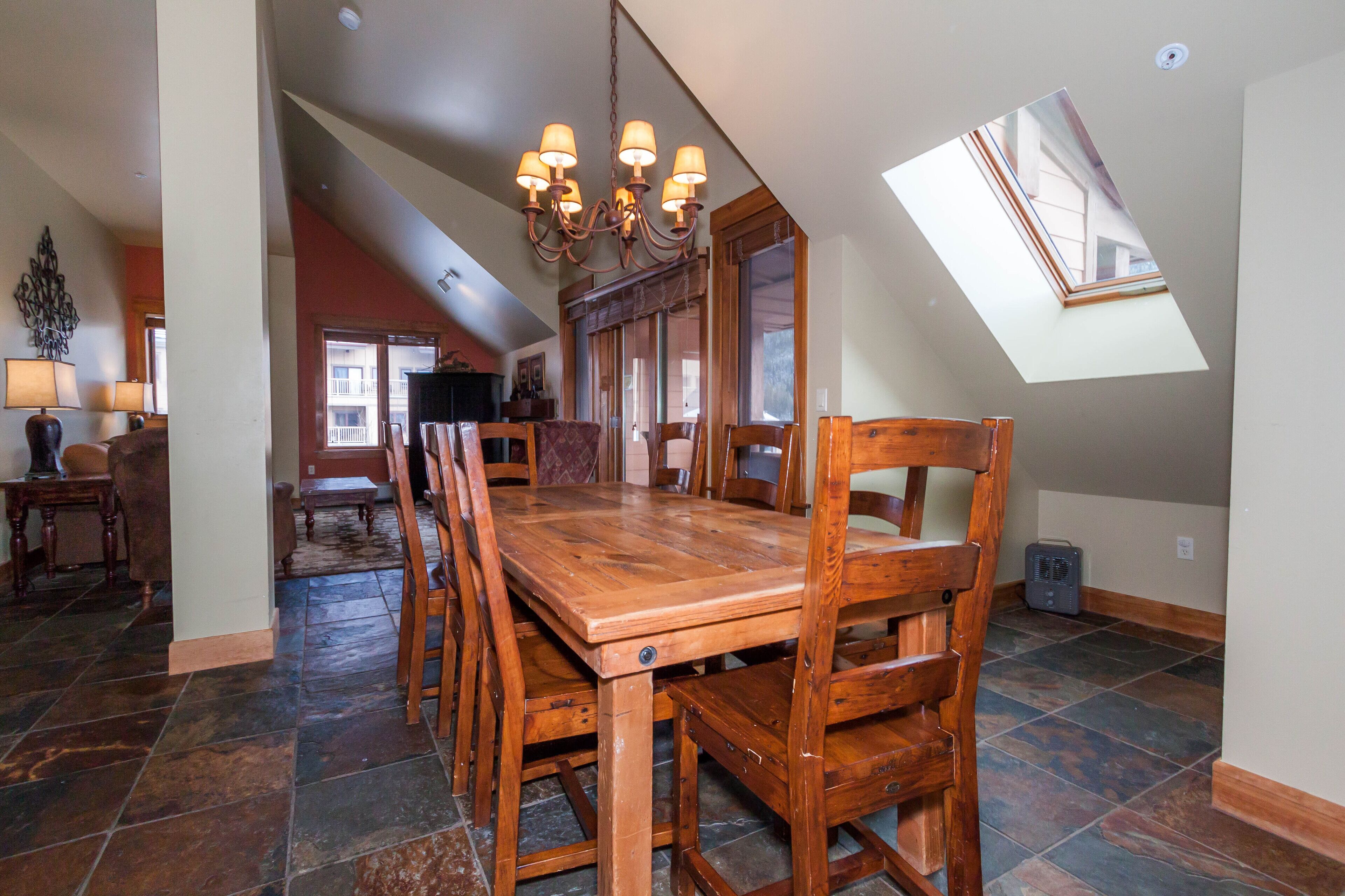 A dining area with a wooden table and chairs, a chandelier, and a view of the outside through a skylight.
