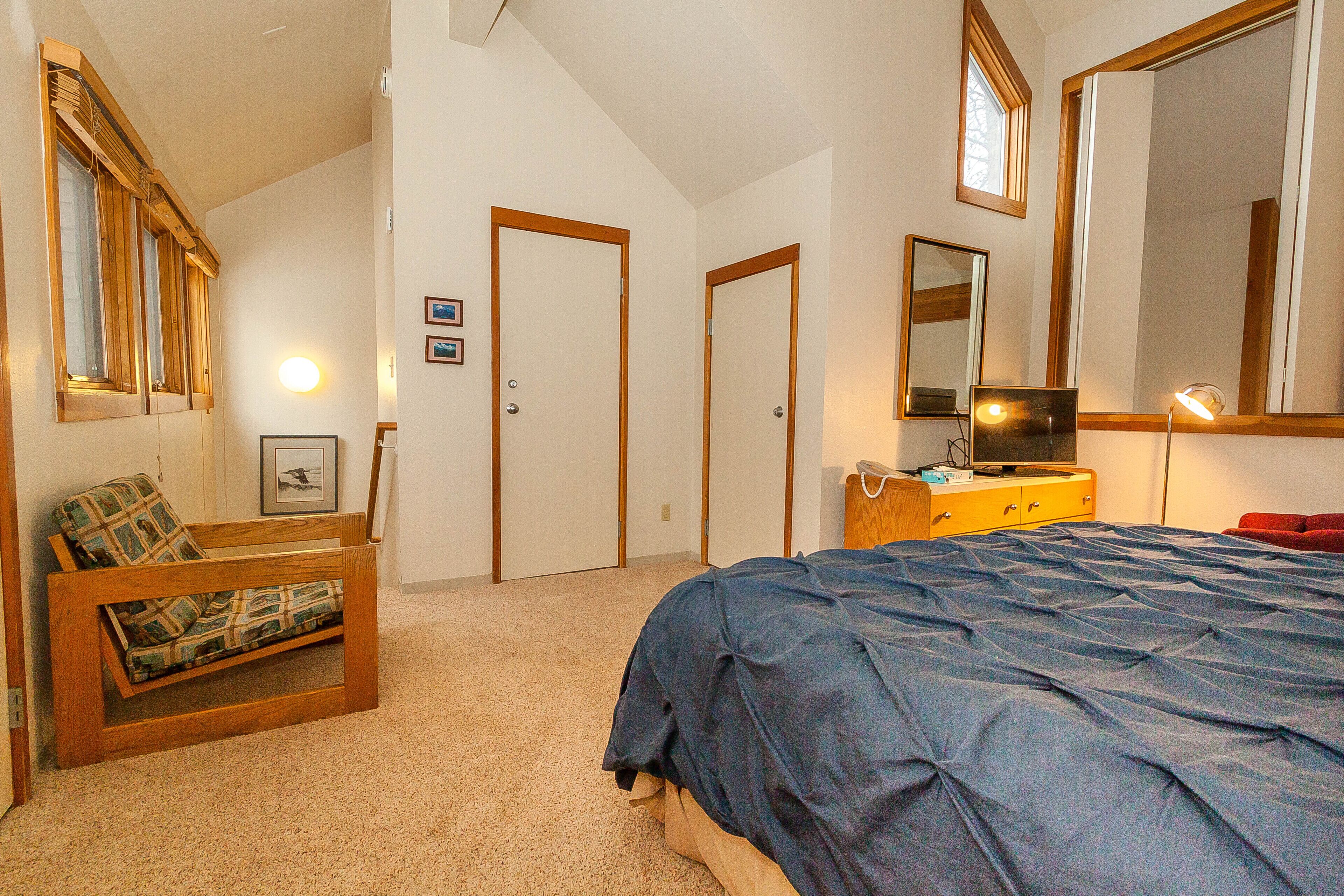 A bedroom with a bed, a wooden bench, a dresser, and a mirror.