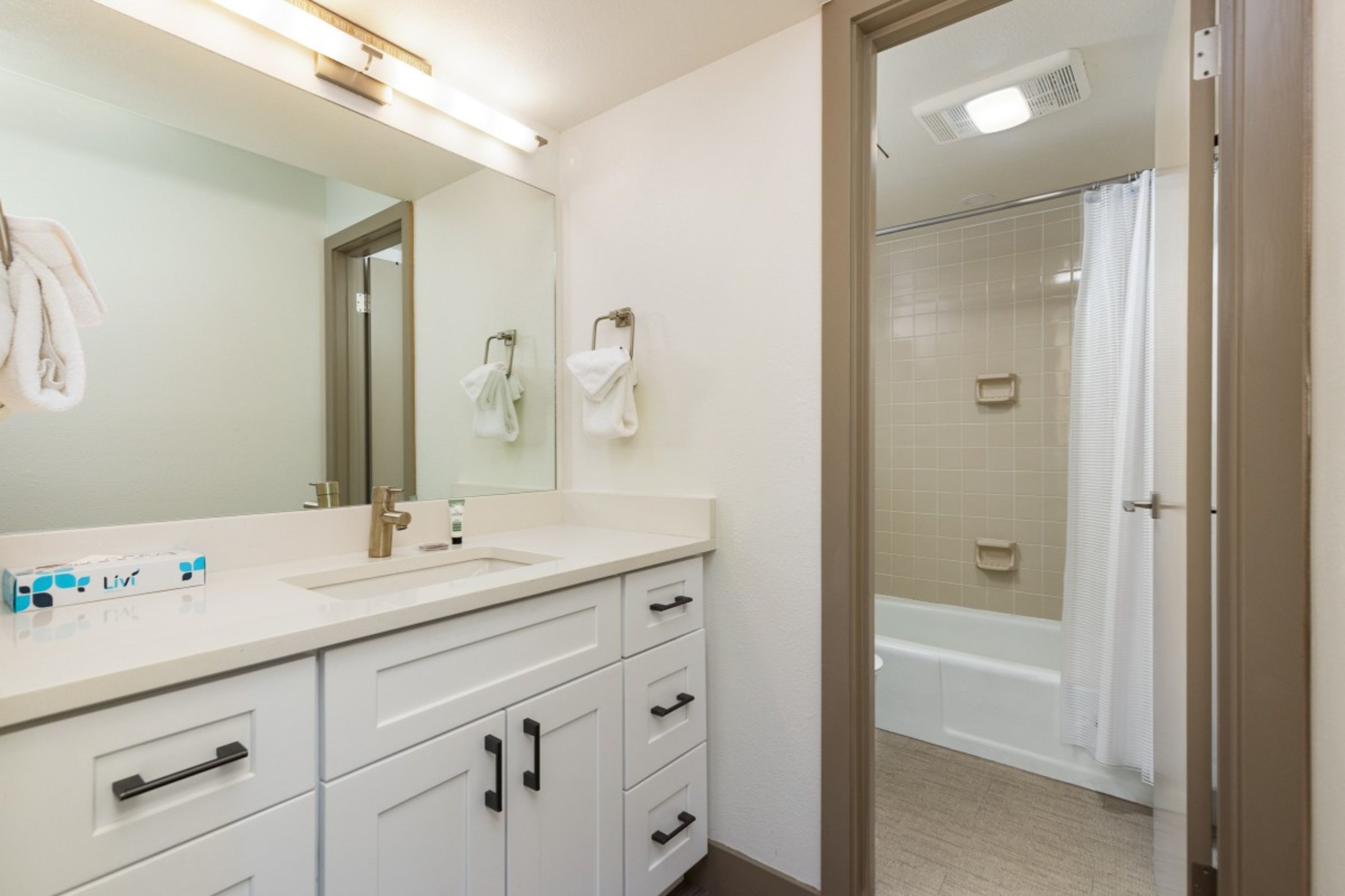 Une salle de bain moderne avec un grand miroir, un meuble-lavabo blanc et un espace douche.