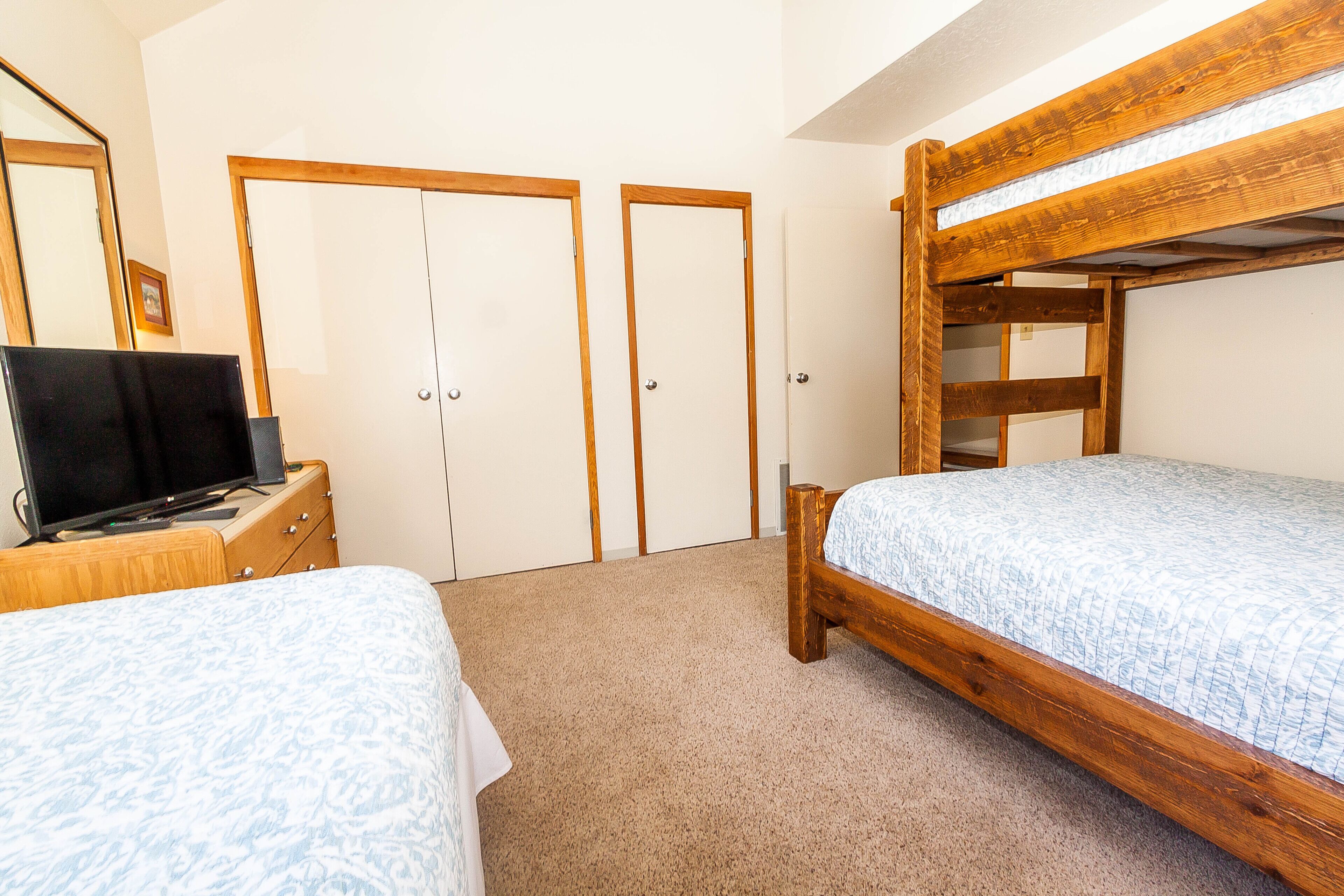 A bedroom with two beds, a TV on a dresser, and wooden bunk beds.