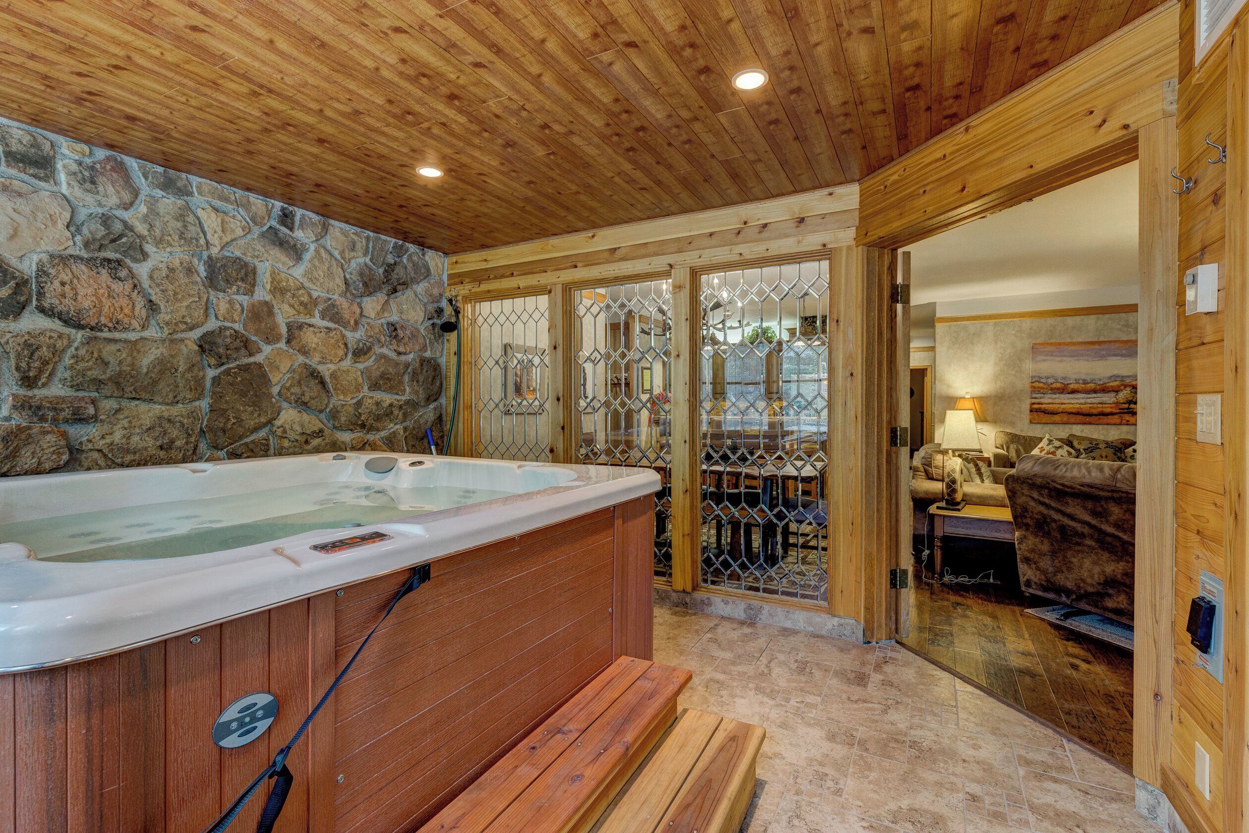 A hot tub in a wooden cabin with stone walls and a cozy seating area.