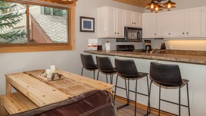 A kitchen with a wooden table, bar stools, a microwave, and a chandelier. - Flying Dutchman by Summit County Mountain Retreats (Keystone)