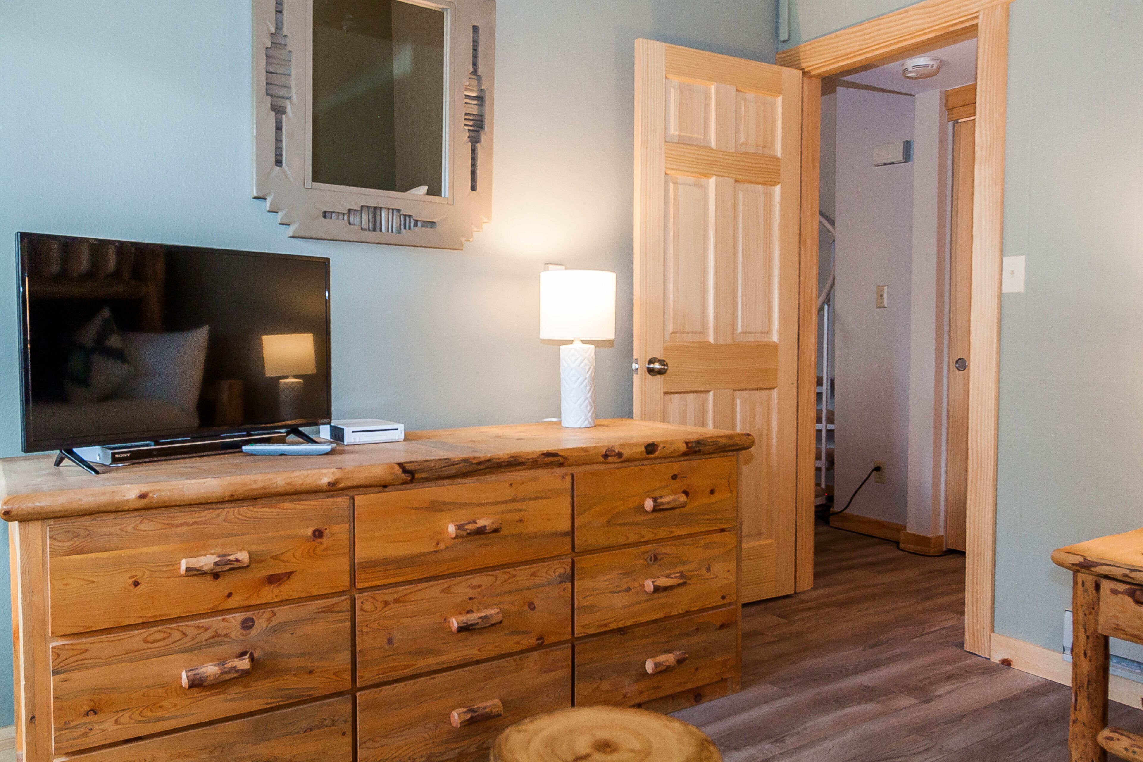 A wooden dresser with multiple drawers, a television on top, and a lamp beside it.