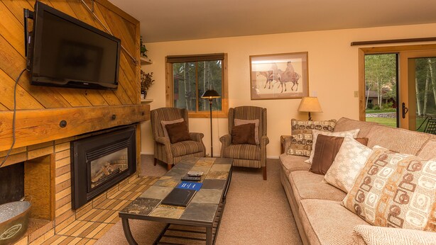 A cozy living room with a fireplace, two armchairs, a sofa, and a television mounted on the wall. - Flying Dutchman by Summit County Mountain Retreats (Keystone)
