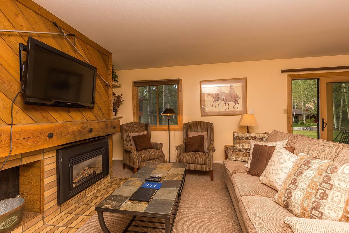 A cozy living room with a fireplace, two armchairs, a sofa, and a television mounted on the wall.