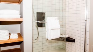 A bathroom with white tiled walls, a glass shower enclosure, and wooden shelves holding folded towels. - Flying Dutchman by Summit County Mountain Retreats (Keystone)