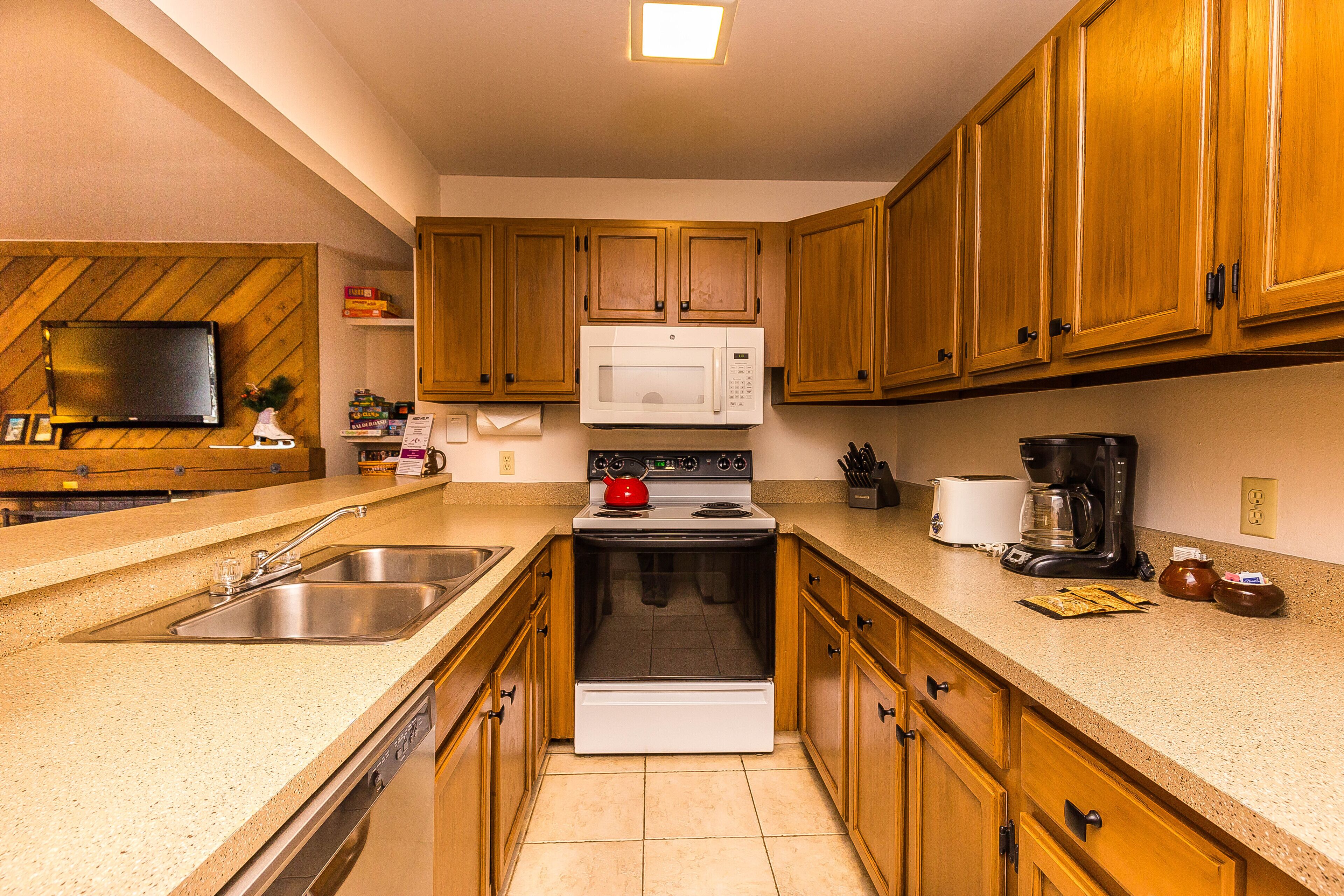 A kitchen with wooden cabinets, a microwave, stove, sink, and a television on the wall.