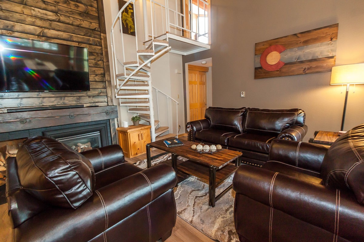 A living room with leather sofas, a wooden coffee table, a fireplace, and a TV mounted on a wooden wall.