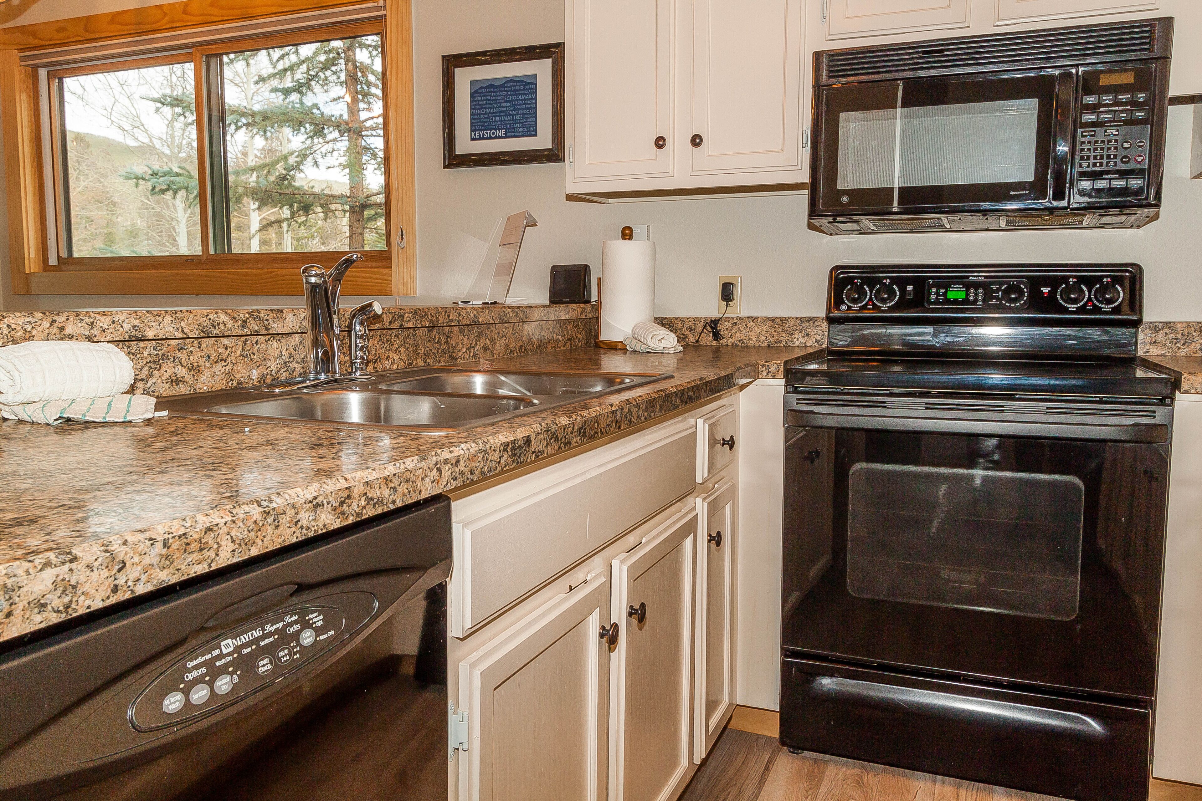 A kitchen with a granite countertop, stainless steel sink, a black stove, and a microwave above it.
