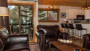 A living room with leather sofas, a wooden coffee table, and a kitchen in the background. - Flying Dutchman by Summit County Mountain Retreats (Keystone)
