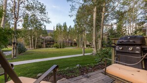 A patio with a grill, chairs, and a view of a lawn and trees. - Flying Dutchman by Summit County Mountain Retreats (Keystone)