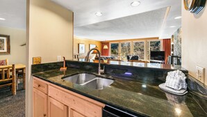 A modern kitchen with a black granite countertop, stainless steel sink, wooden cabinets, and a stone backsplash. - Decatur #1787 by Summit County Mountain Retreats (Keystone)