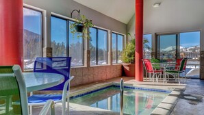 An indoor pool area with a view of mountains, a table with chairs, and a hanging plant. - Decatur #1787 by Summit County Mountain Retreats (Keystone)