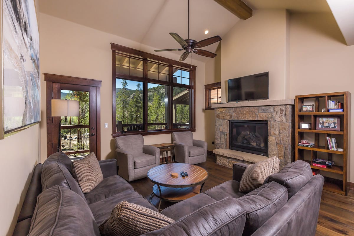 A living room with a stone fireplace, leather sofas, a coffee table, and a television mounted above the fireplace.