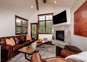 A spacious living room with a stone fireplace, leather sofas, and large windows offering a view of the outdoors. - Alders #801 (Keystone)