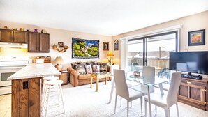 A modern kitchen with a marble island, a dining area with a glass table, and a living room with a sofa and a TV. - Dillon Valley East by Summit County Mountain Retreats (Dillon)