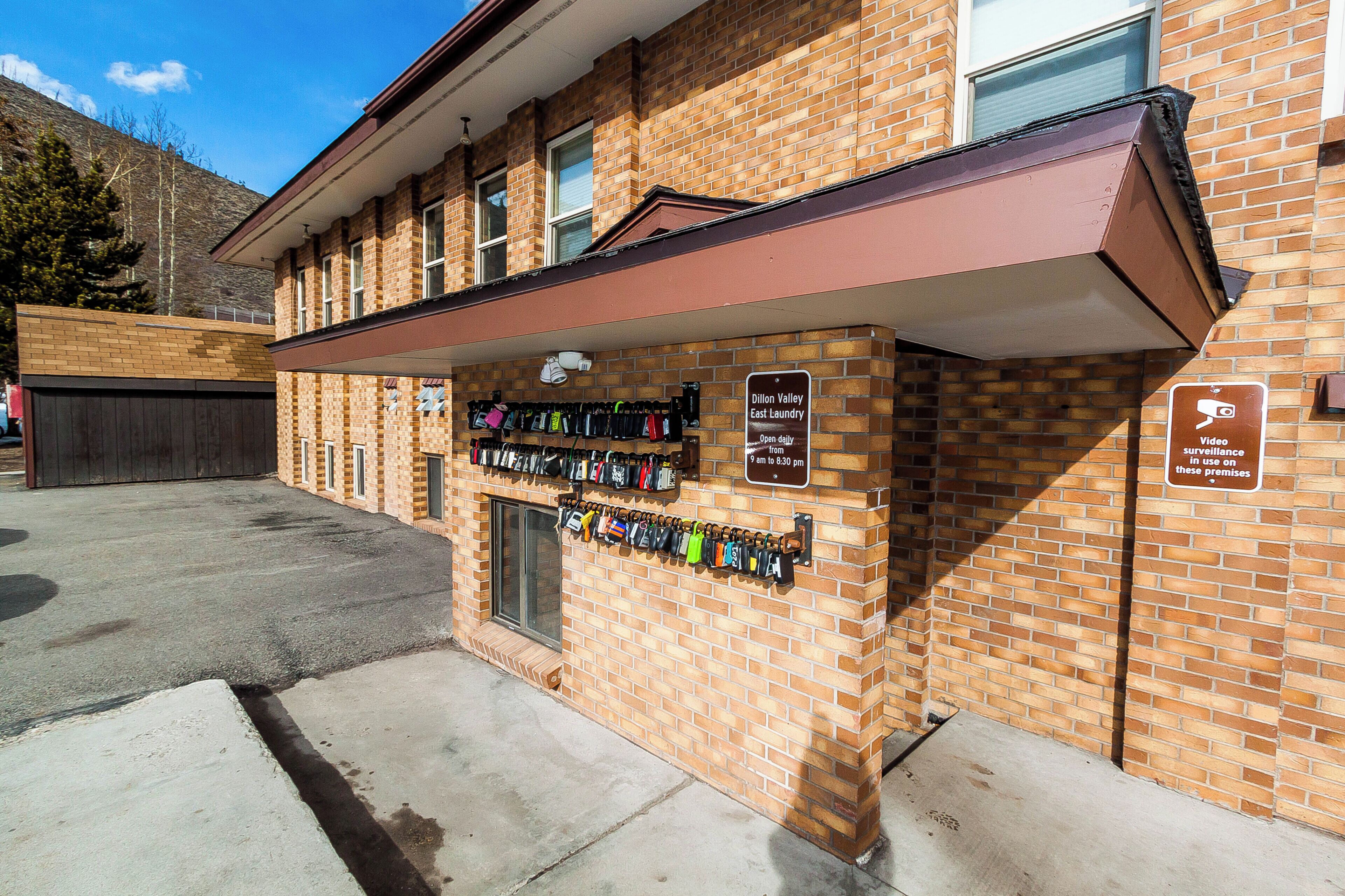 A brick building with a row of keys hanging on the wall, a sign for 'Dillon Valley East Laundry' open daily, and a 'Video surveillance' sign.