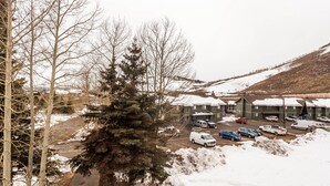 A snow-covered parking lot with several vehicles, including a white truck and a blue car, in front of a building with a green roof and multiple windows. - Dillon Valley East by Summit County Mountain Retreats (Dillon)