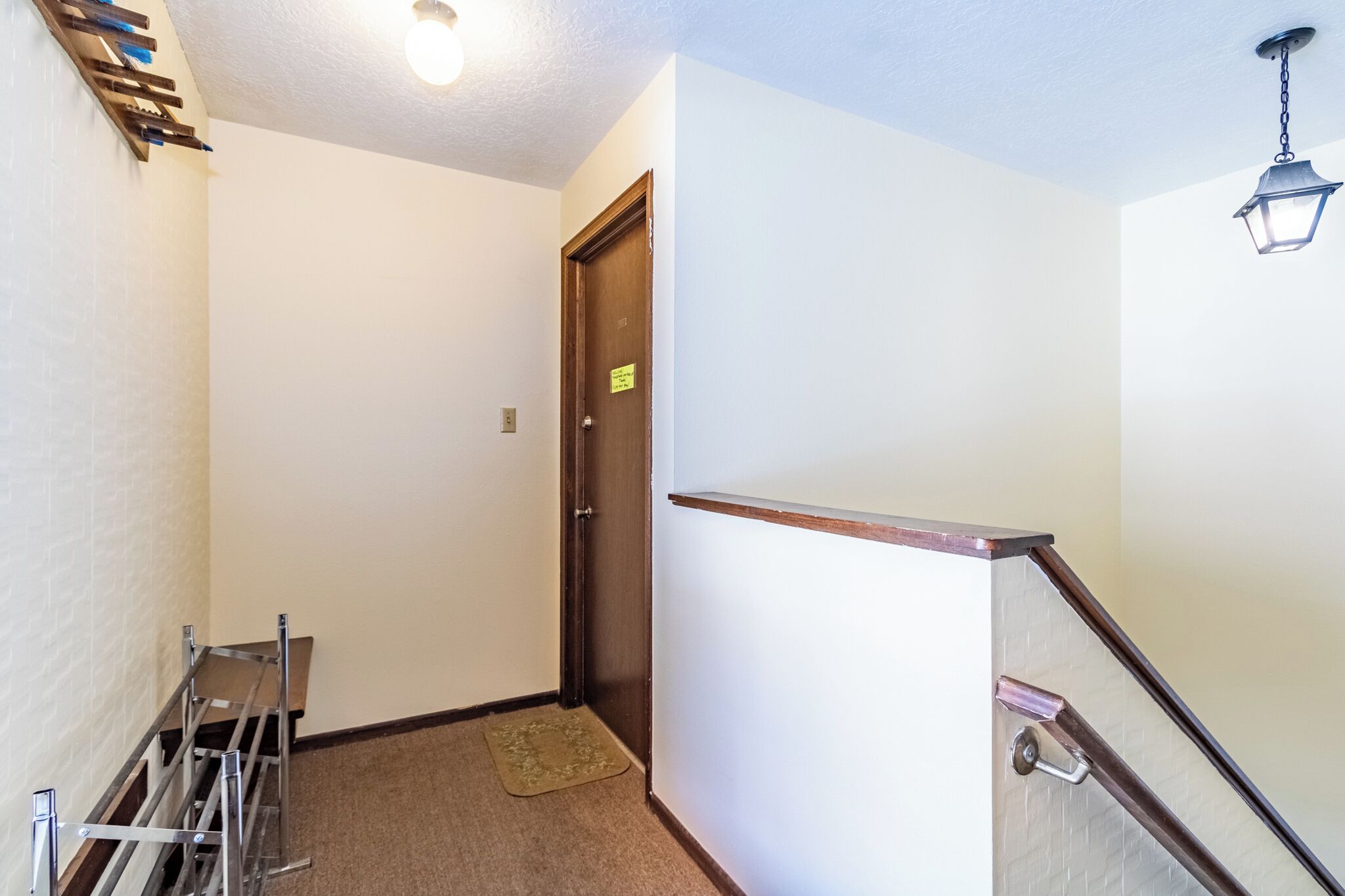 A hallway with a wooden door, a metal rack, and a carpeted floor.