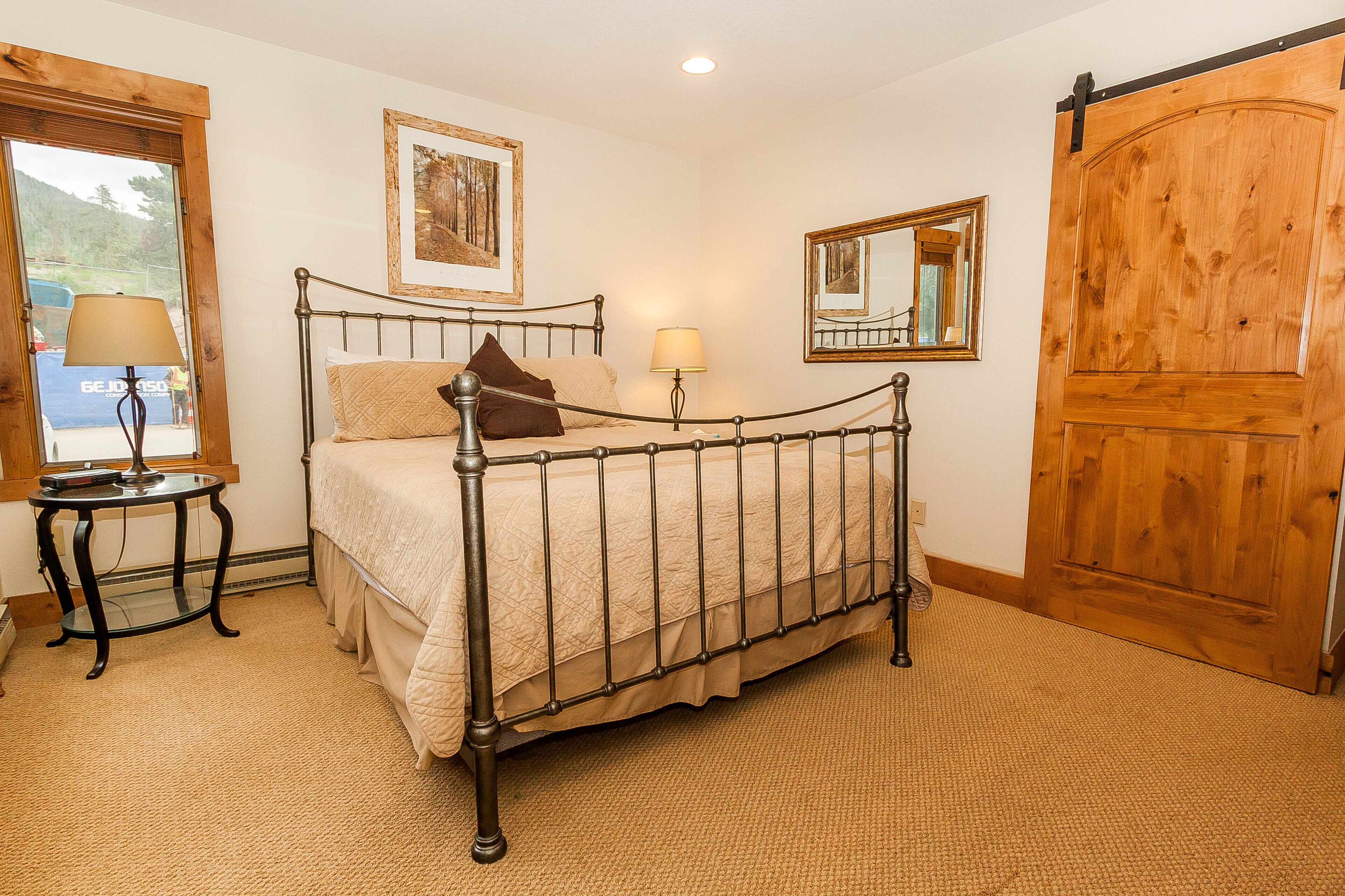 A bedroom with a metal bed frame, two bedside tables with lamps, a wooden door, and a large mirror.
