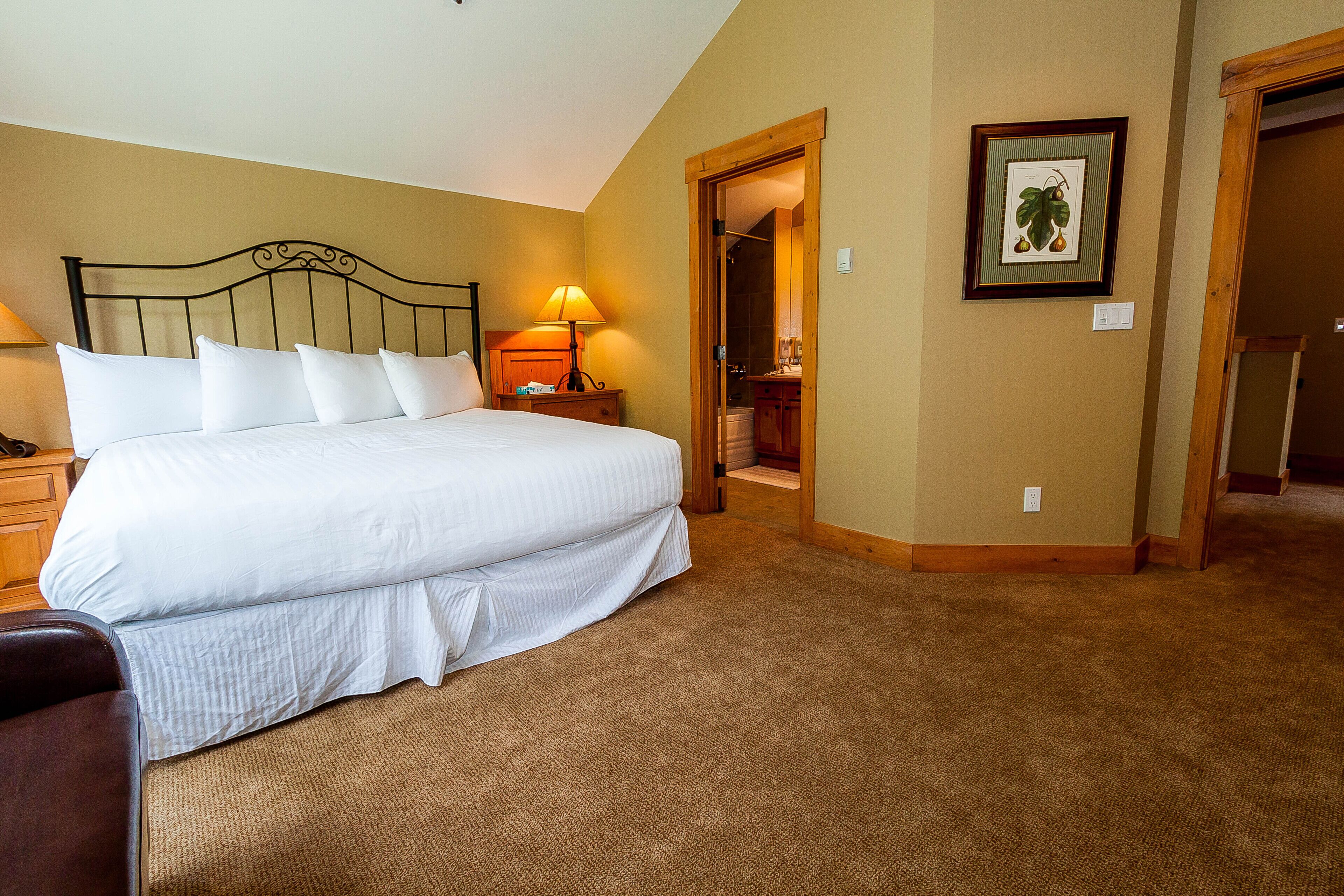 A neatly made bed with white linens, a wooden headboard, and a bedside lamp.