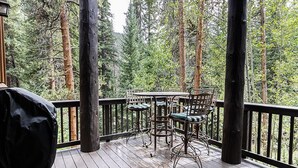 A wooden deck with a table and chairs, surrounded by tall trees. - Trapper's Crossing #8770 by Summit County Mountain Retreats (Keystone)