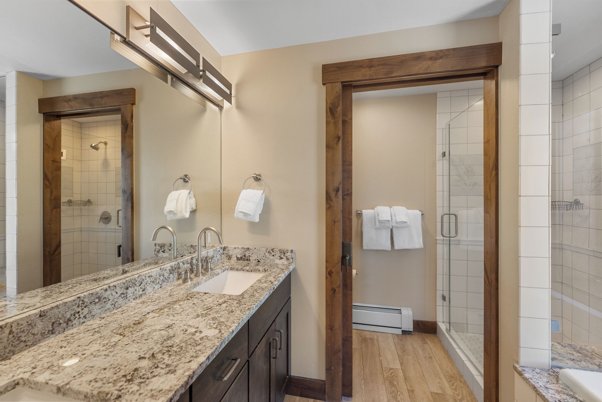 Un baño moderno con lavamanos de granito, puerta de madera y cabina de ducha de vidrio.