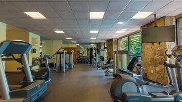 Ein Fitnessstudio mit verschiedenen Trainingsgeräten, einer Steinwand und großen Fenstern.