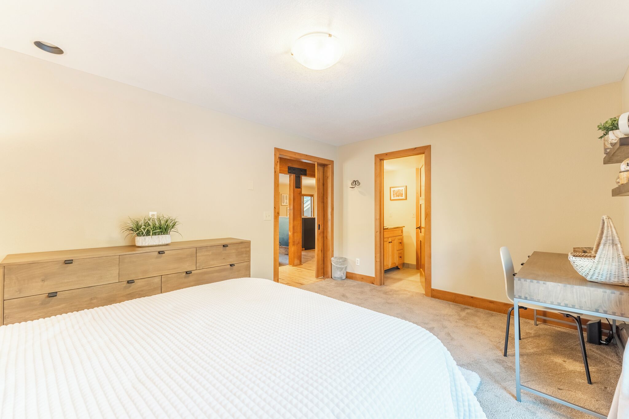 A bedroom with a large bed, wooden dresser, and a small table with a chair.