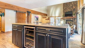 A spacious kitchen with a large island, wooden beams, a stone accent wall, a fireplace, and a television. - Enclave #34 by Summit County Mountain Retreats (Keystone)