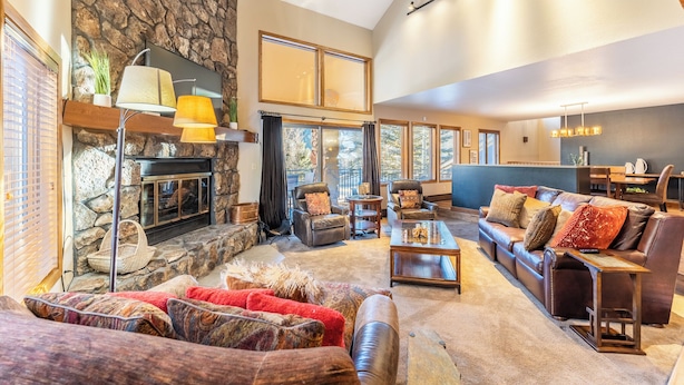 A spacious living room with a stone fireplace, leather sofas, and a large window overlooking a scenic view. - Enclave #34 by Summit County Mountain Retreats (Keystone)