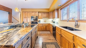 A modern kitchen with wooden cabinets, granite countertops, a built-in oven, and a large window with blinds. - Enclave #34 by Summit County Mountain Retreats (Keystone)