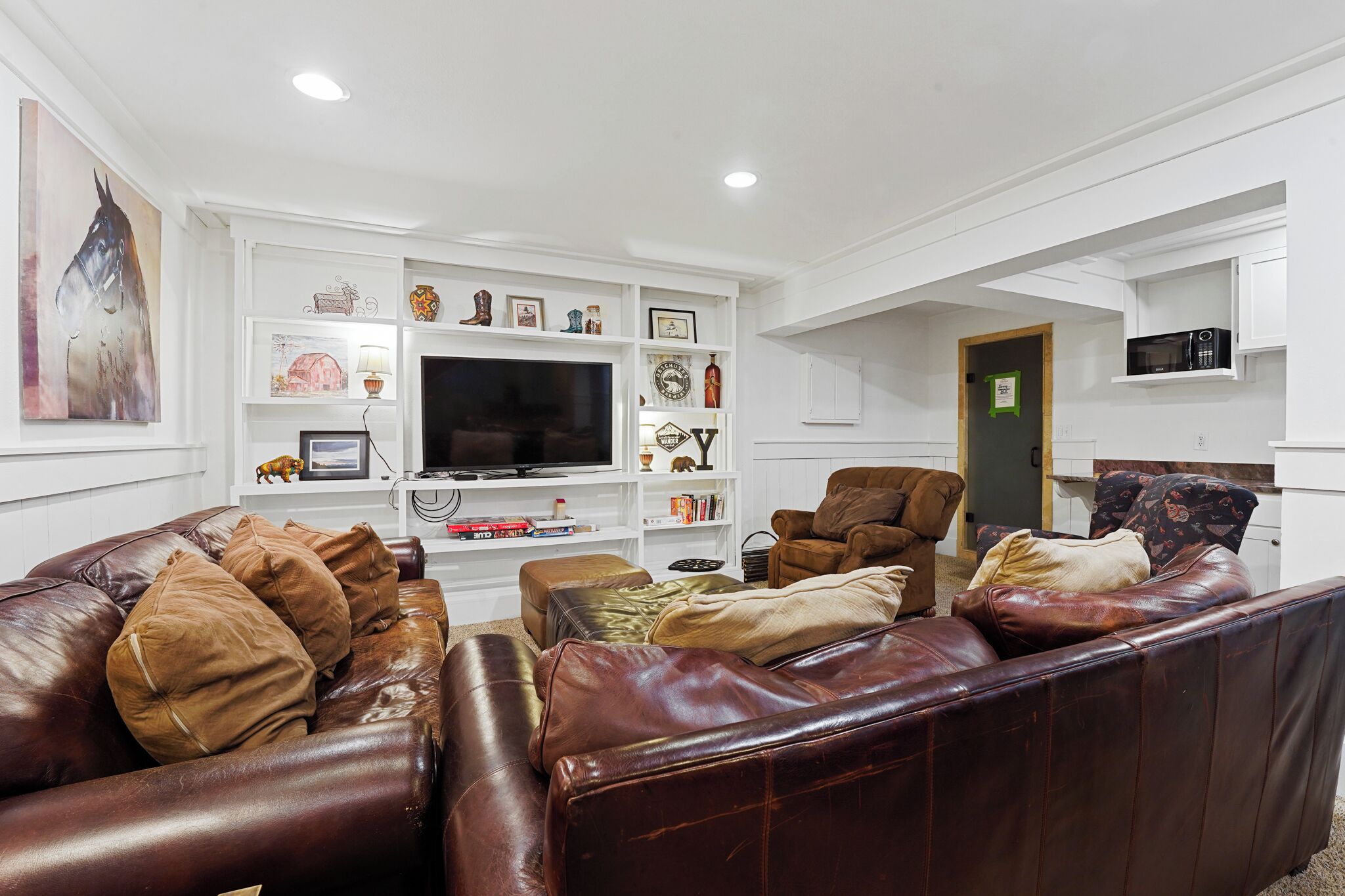 A living room with a brown leather sofa, a television, and various decorative items on shelves.