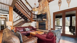 A spacious living area with a stone fireplace, leather sofas, and a wooden staircase. - Soda Ridge 1608 by Summit County Mountain Retreats (Keystone)