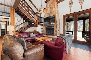 A spacious living area with a stone fireplace, leather sofas, and a wooden staircase.