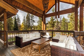 A covered outdoor seating area with a wooden ceiling, wicker furniture, and a view of a forest. - Soda Ridge 1608 by Summit County Mountain Retreats (Keystone)