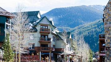 A multi-story building with a balcony, surrounded by trees and mountains in the background.