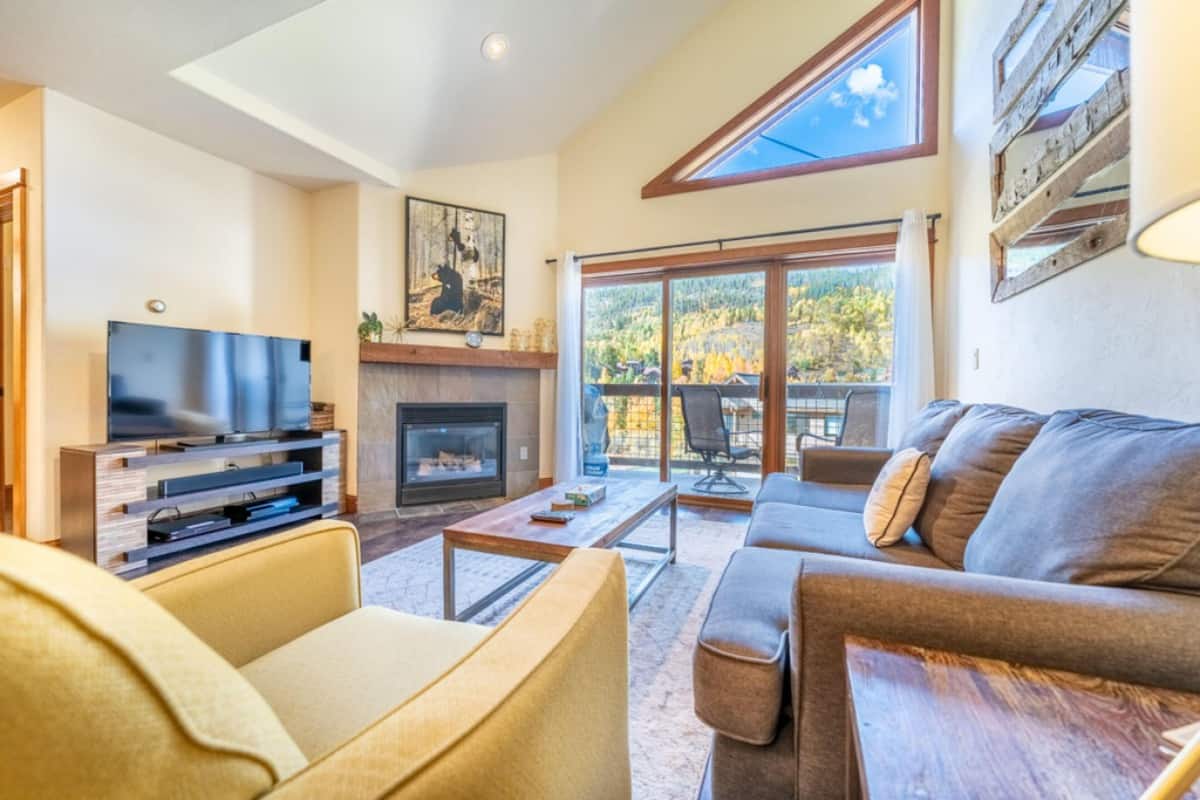 A modern living room with a fireplace, a television, and a large window overlooking a scenic view.