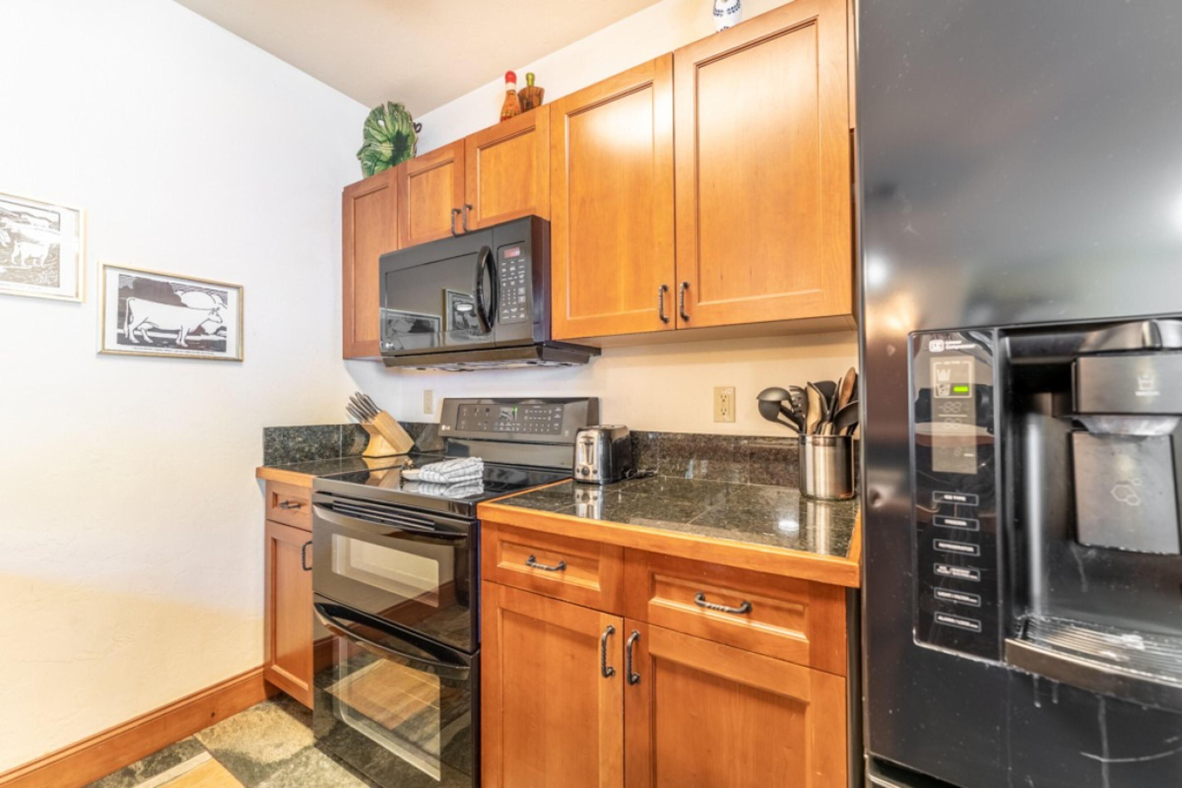 A kitchen with wooden cabinets, a microwave, an oven, and a refrigerator.