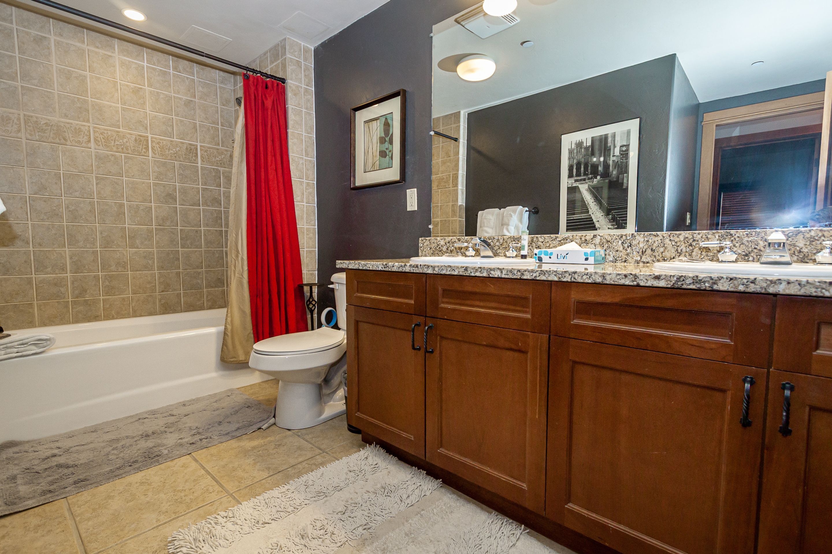 A bathroom with a bathtub, toilet, wooden cabinets, and a large mirror.