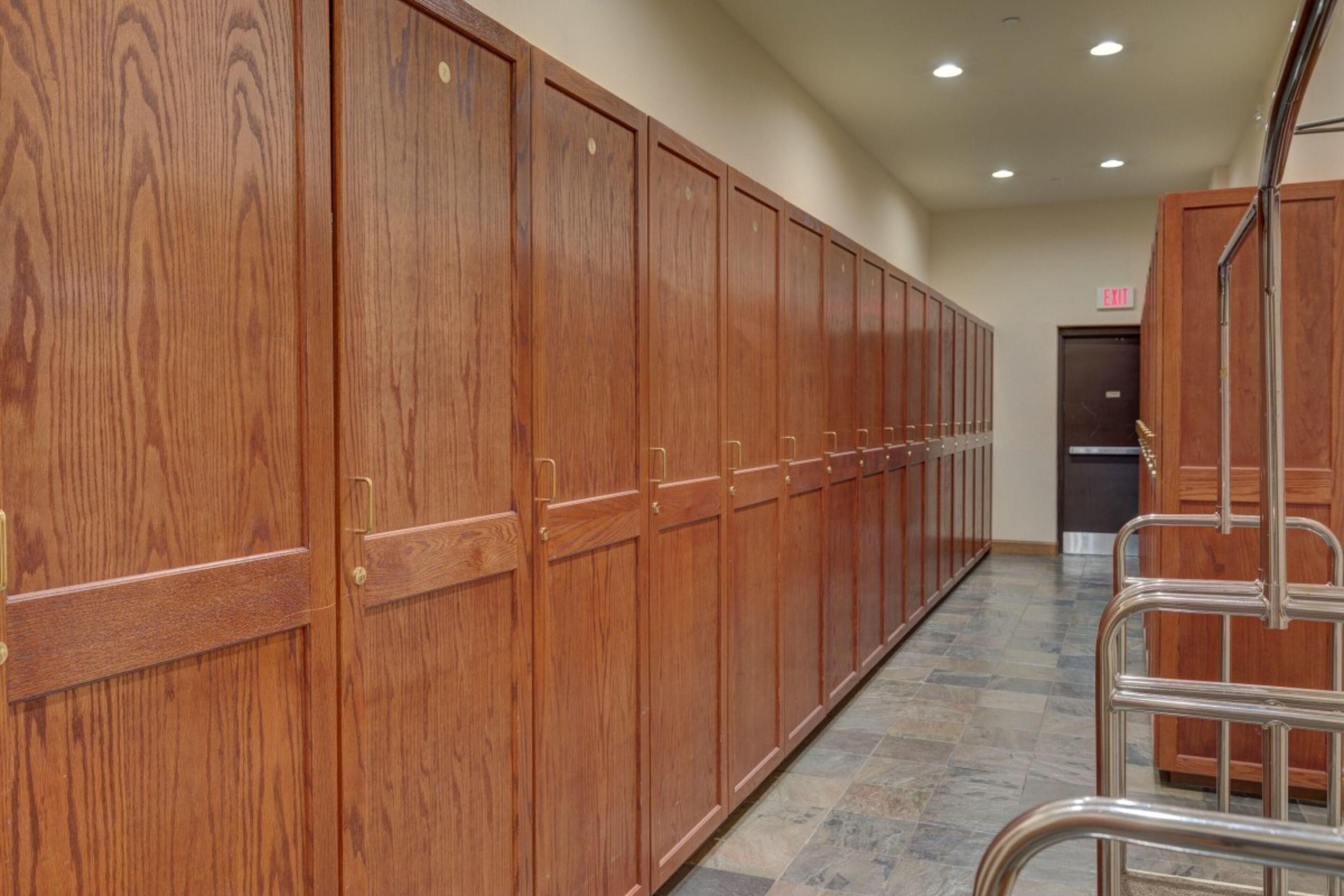 A row of wooden lockers with metal handles, a tiled floor, and a metal chair.