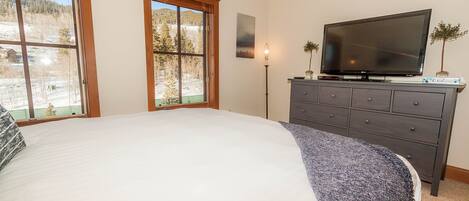 Camera da letto con un letto grande, una cassettiera, una TV a schermo piatto e due finestre con vista su un paesaggio innevato.