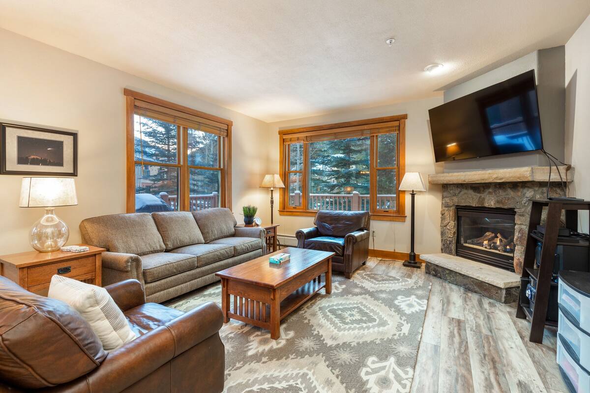 A cozy living room with a fireplace, comfortable seating, and large windows.