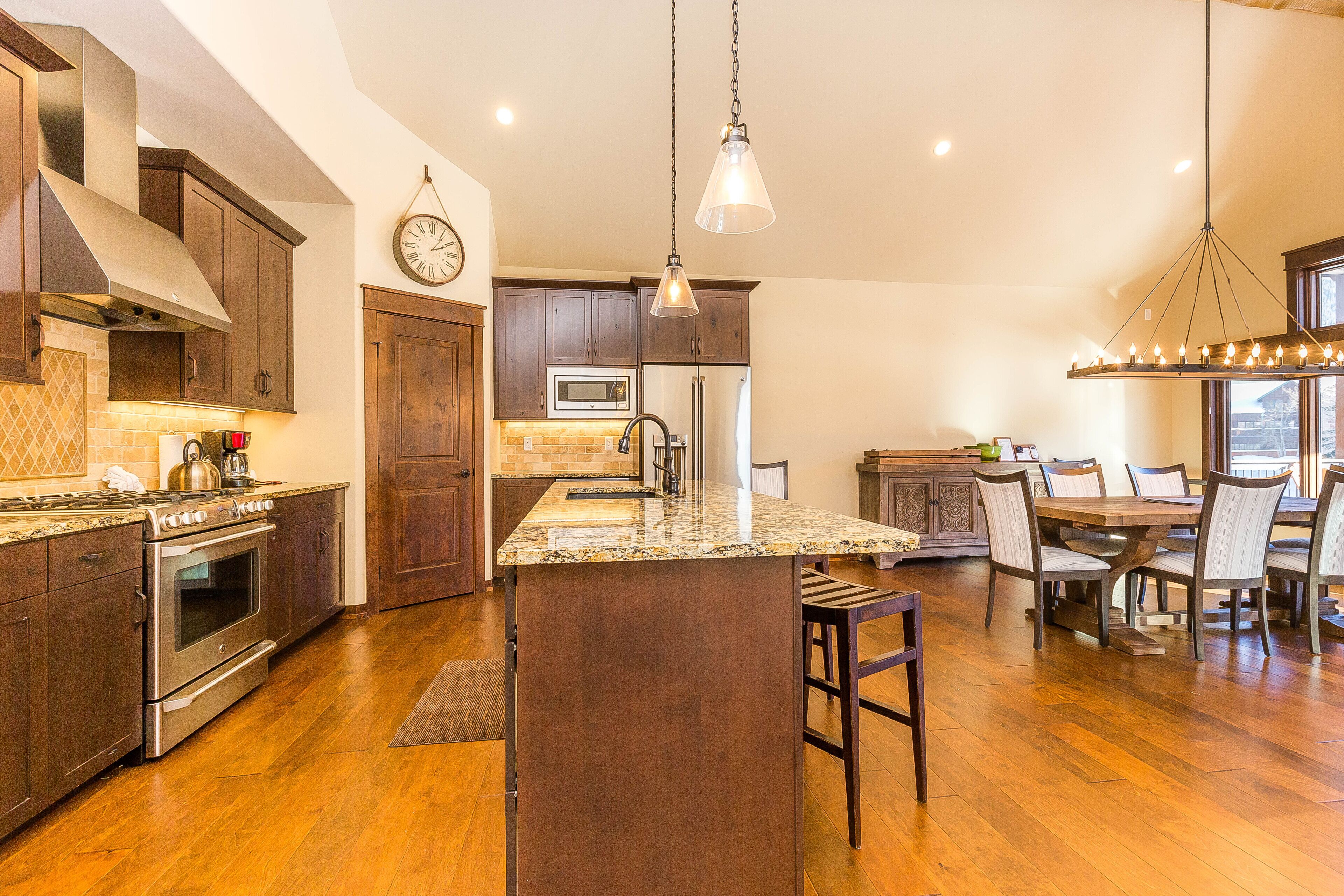 Una cocina amplia con armarios de madera, una isla central, electrodomésticos de acero inoxidable y un comedor con sillas y una mesa.