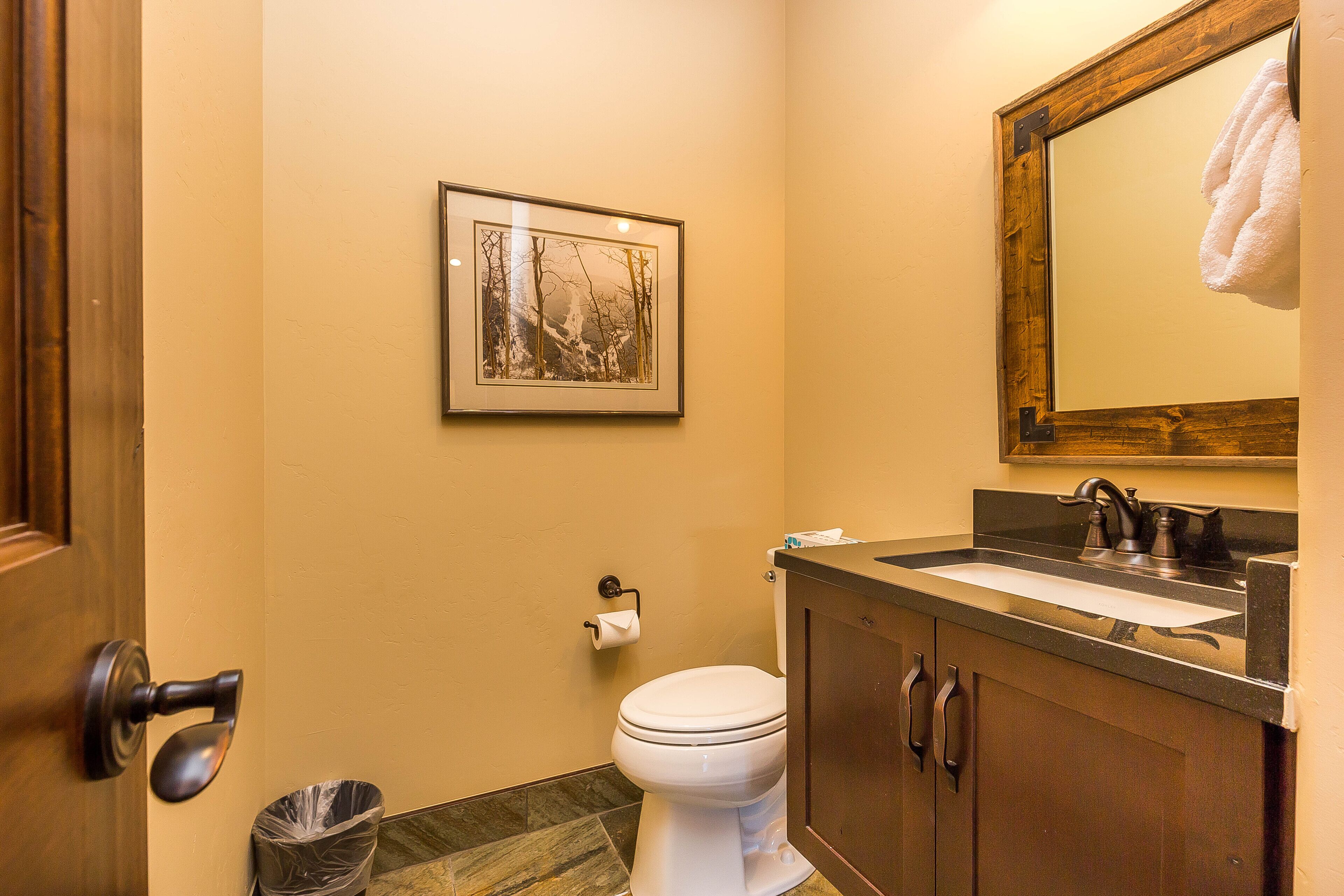 Une salle de bain équipée de toilettes, d’un lavabo, d’un miroir et d’un tableau encadré au mur.