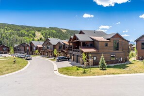 A modern residential area with wooden houses, a curved driveway, and a hilly forested background. - River Run Townhomes by Summit County Mountain Retreats (Keystone)