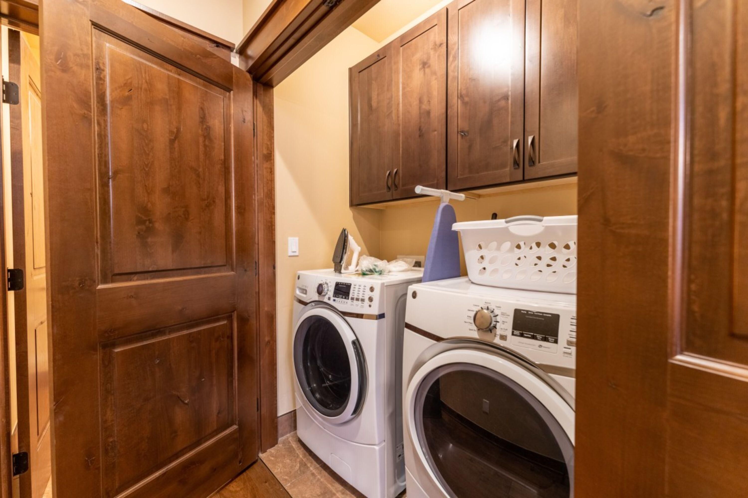 A laundry room with two washing machines and wooden cabinets.