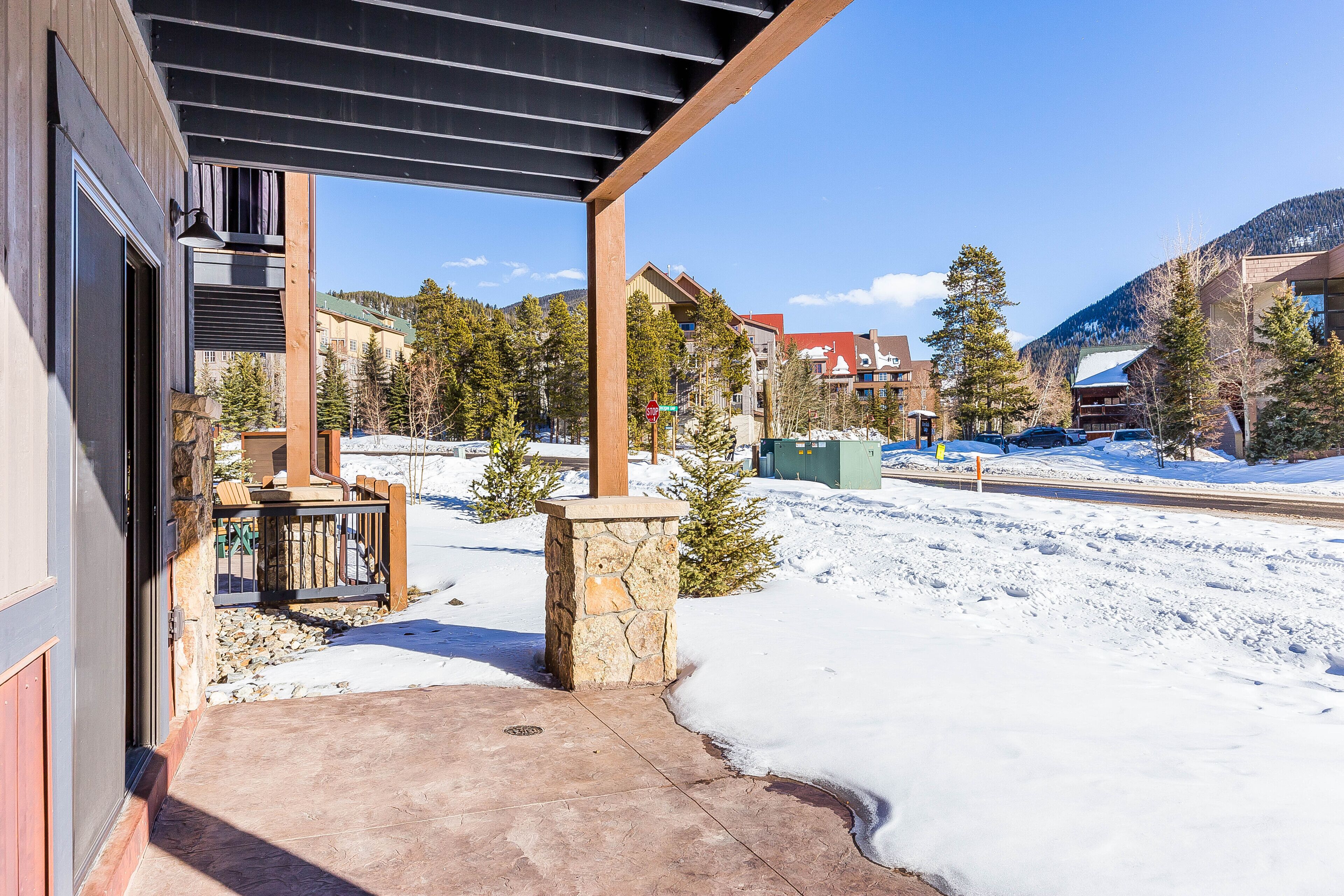 A covered outdoor area with a stone pillar, a wooden deck, and a view of a snowy mountain landscape.
