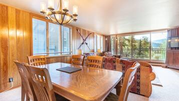A dining area with a wooden table and chairs, a chandelier, and large windows offering a view of the outdoors.