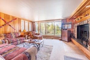 A cozy living room with a fireplace, large windows, and a ski rack on the wall. - Pines #2059 (Keystone)